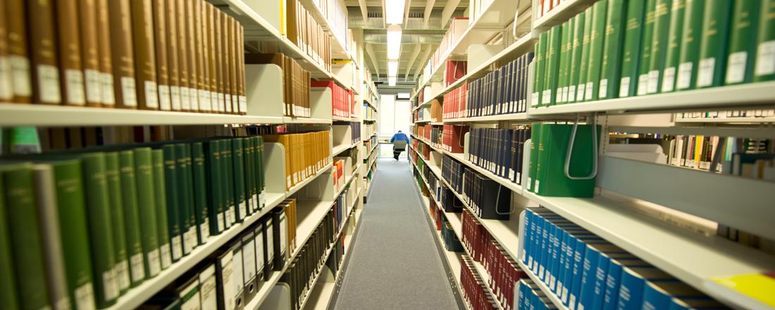 Student sitzt in der Bibliothek der Uni Bayreuth zwischen zwei langen Bücherreihen und liest.
